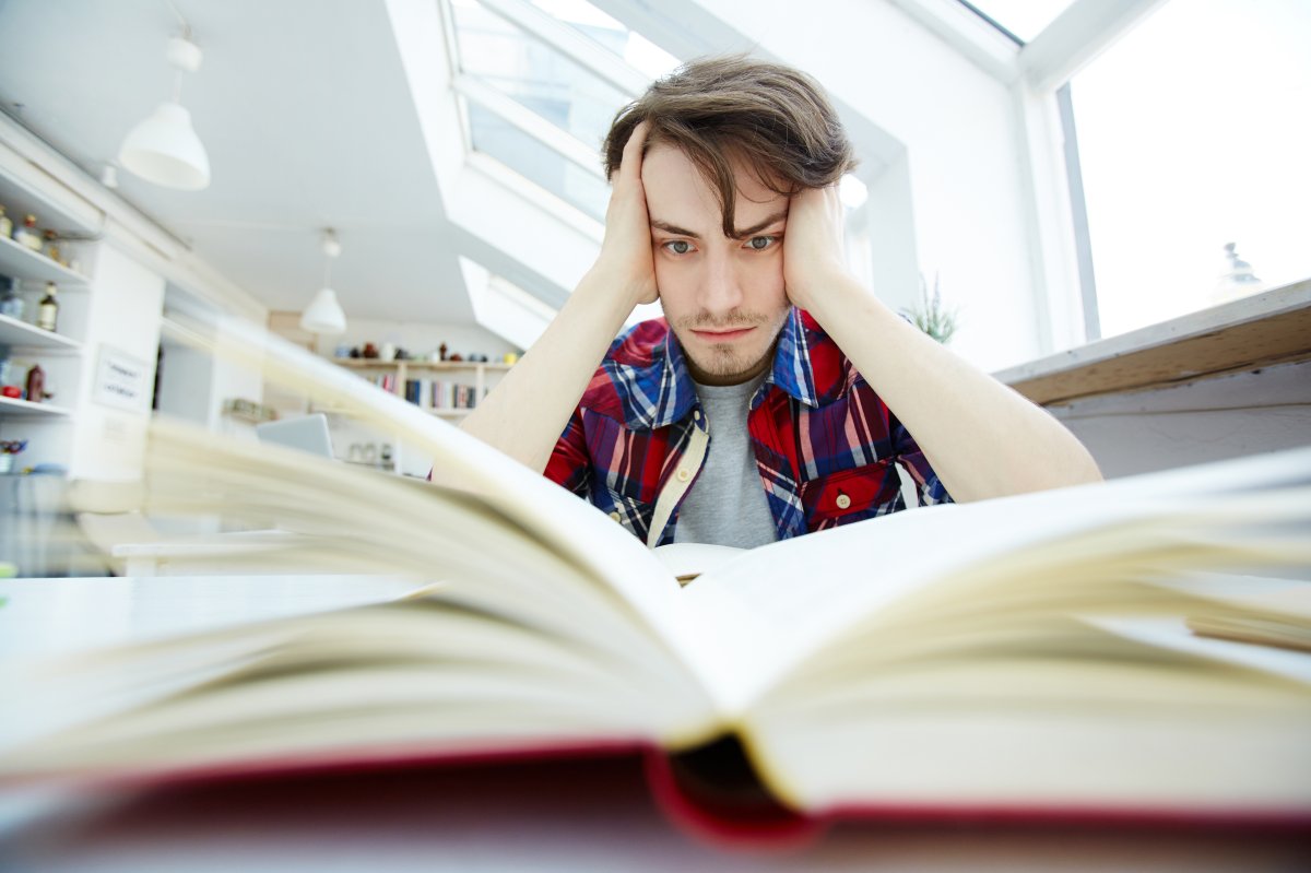 Étudiant en surcharge mentale – Stress scolaire et perte de confiance en soi Jeune adulte assis à un bureau, entouré de livres et d’un ordinateur, visiblement en détresse mentale, représentant le stress scolaire, la pression académique et le manque de confiance